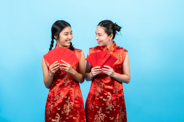 肖像，女人，穿着红色的旗袍在中国新年，拿着几个红包红包，交给姐妹们，直到全部消失，孤立的室内工作室在粉红色的背景。图片下载