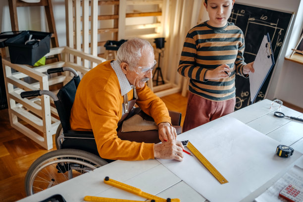 男孩在他的木工作坊里帮助坐轮椅的爷爷图片下载