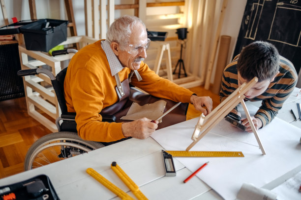 男孩在他的木工作坊里帮助坐轮椅的爷爷图片下载