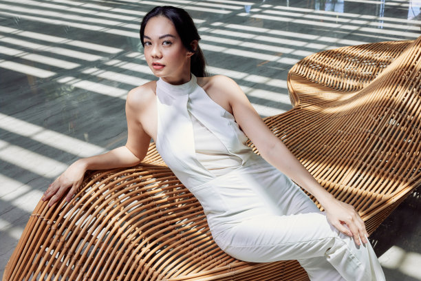 亚洲年轻漂亮的女人坐在现代木椅上，对几何阴影和线条的极简主义室内摆姿势图片下载