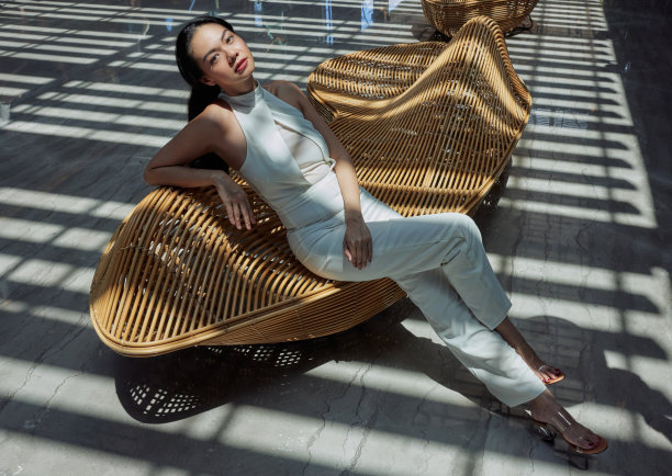 亚洲年轻漂亮的女人坐在现代木椅上，对几何阴影和线条的极简主义室内摆姿势图片下载