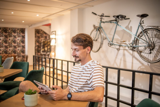 一个年轻的潮人坐在咖啡馆里，看着他的平板电脑图片下载