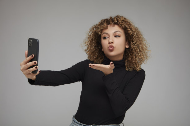 一名年轻卷发女子正在用手机进行视频通话，她向面前的人飞吻。图片下载