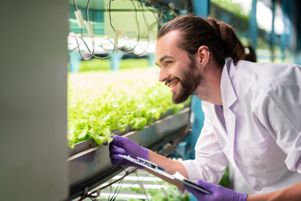 男科学家穿着白色制服，在室内垂直农场的有机水培蔬菜地里工作，开心地笑着，分析和研究有机蔬菜图片下载