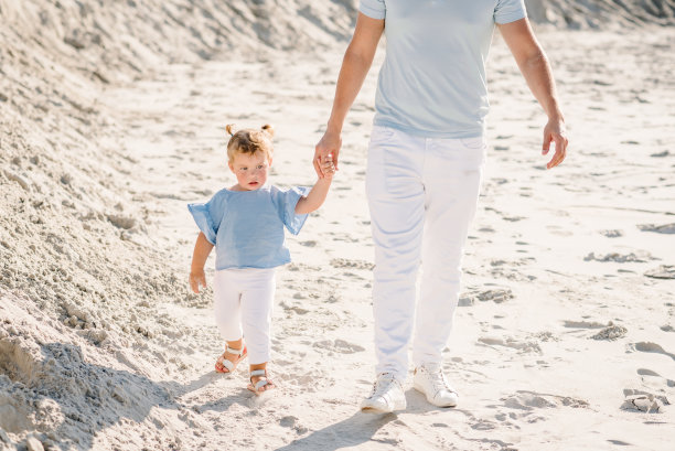 父亲和女儿。爸爸牵着小孩的手走在沙滩上。父亲节。家庭和童年概念。腿的底部视图。图片下载