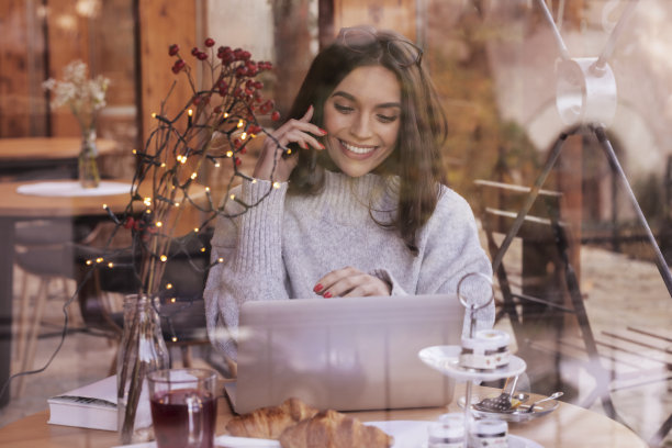 快乐的年轻女子讲她的手机，坐在咖啡馆里图片下载