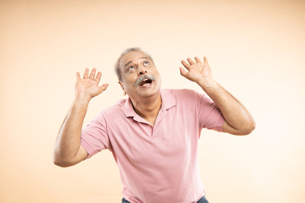 高级印度人害怕，他的手臂像什么东西从上面落下的姿态孤立在米色背景。图片下载