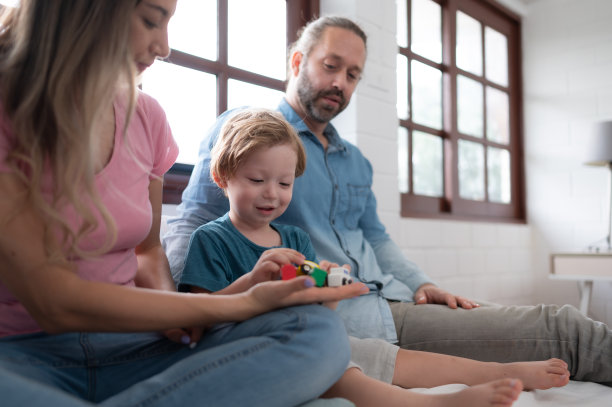 爸爸妈妈带着小男孩一起在卧室里玩你的新玩具。增强儿童思维能力的玩具。图片下载
