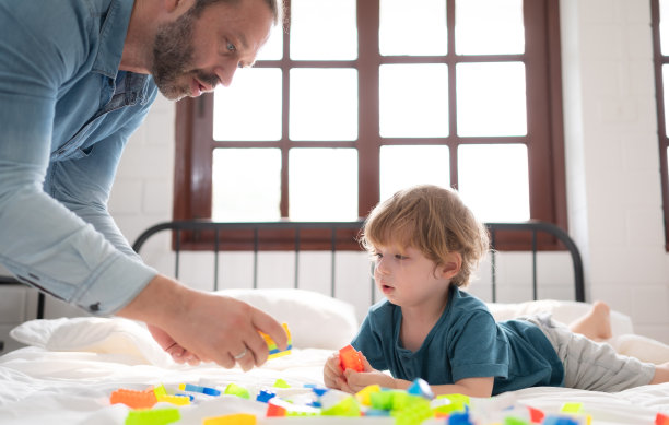 爸爸和小男孩一起在卧室里玩你的新玩具。增强儿童思维能力的玩具。图片下载
