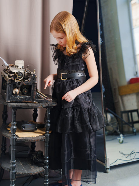 可爱的金发少女扎着辫子，穿着黑色连衣裙，用复古打字机打印图片下载