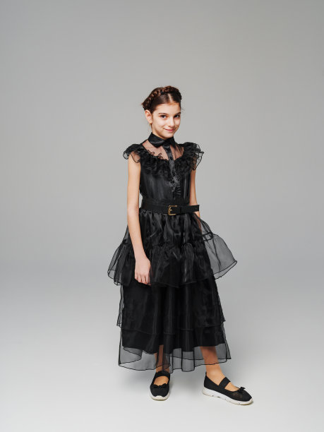 可爱的少女辫子在黑色的长曲线连衣裙上的灰色背景。图片下载