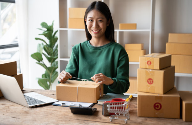 年轻女子包装产品的客户与纸箱在家里，业务在线航运和交货的概念。图片下载