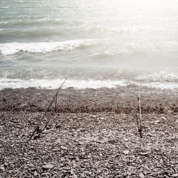 旋转杆站在海边卵石海滩的岸边，在海浪汹涌的狂风中等待大鱼的咬一口图片下载