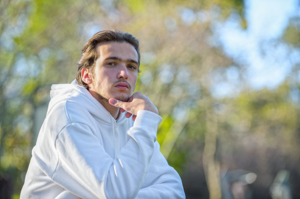 近距离的肖像，英俊的年轻人在公园在夏天。自信的男人望着镜头，户外写真。一个棕色头发的男模特平静的脸。一个表情严肃的家伙图片下载