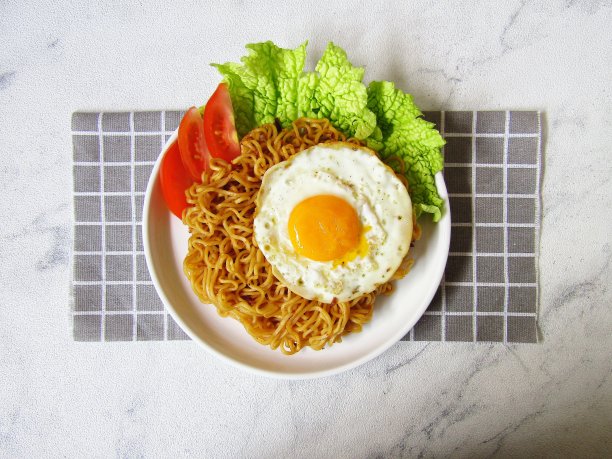 Mie Sedap Goreng，是一种印尼即时炒面，除了Indomie Goreng外，它也很受欢迎。盛在白色盘子里，鸡蛋、西红柿和白菜朝上。在方形餐巾上。图片下载