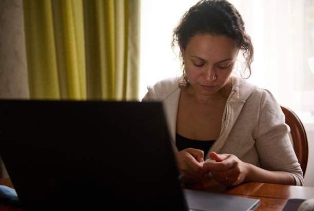 年轻女子在笔记本电脑上工作时阅读药物眼药水的使用说明。眼科的概念图片下载