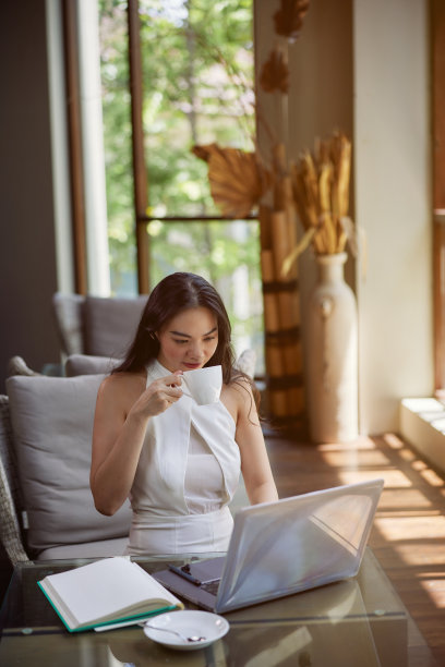 年轻美丽的亚洲女子喝咖啡时使用笔记本电脑，坐在办公室，咖啡馆或联合办公空间。电话会议，在线学习或工作图片下载