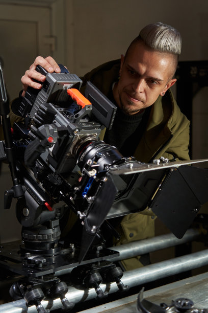 一位英俊的白人摄像师倾斜着专业的电影摄像机，在监视器上监视着拍摄过程。摄像机安装在操作员轨道和手推车上图片下载