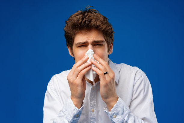 一个年轻人对着蓝色背景的餐巾打喷嚏图片下载