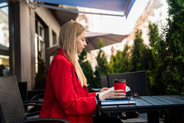 在露台上的咖啡馆里，一名穿着夹克的年轻女子正在使用上网本。图片下载