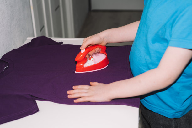 男孩用玩具熨斗熨t恤的特写镜头图片下载