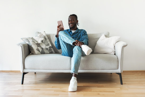 一名非裔美国男子坐在室内沙发上用手机发短信图片下载