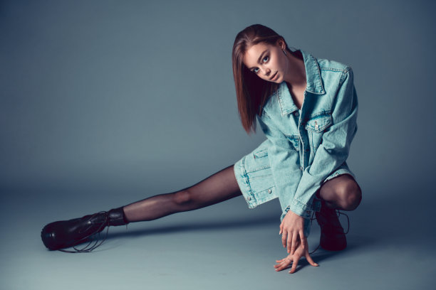 穿着牛仔夹克的美女蹲在灰色的背景附近图片下载