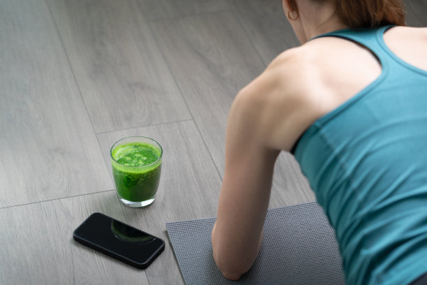 女人在锻炼，在灰色的垫子上躺着。背景里有冰沙排毒。健康的生活，节食的生活方式。图片下载