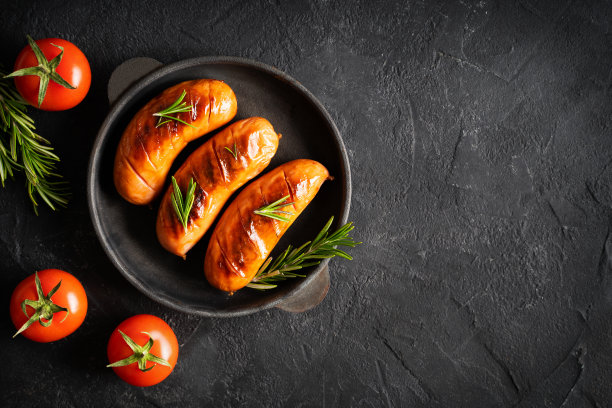 在平底锅里烤烤香肠，黑色背景上放上西红柿图片下载