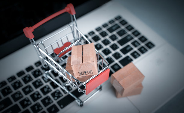网上购物，送货上门。棕色纸盒在购物车与笔记本电脑键盘在桌子办公室。消费者只需指尖即可轻松购物。电子商务和客户体验概念。图片下载