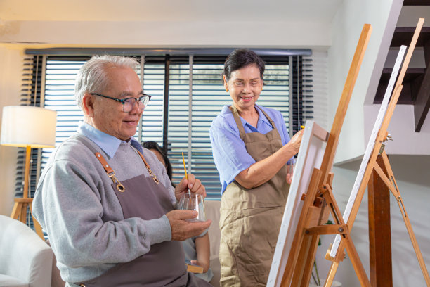 夫妇老年绘画艺术。侧面视图的白发老年妇女持有调色板绘画图片在画架在艺术工作室。图片下载