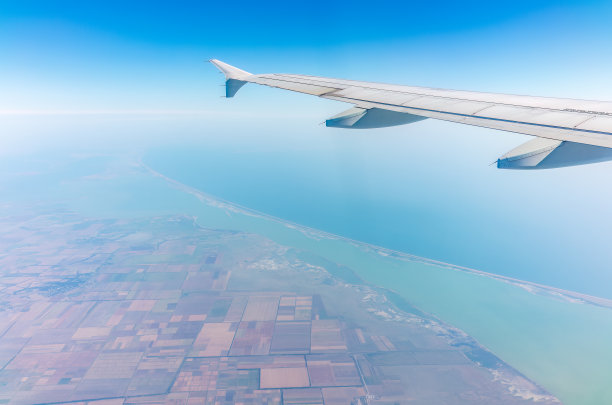 从飞机的窗口可以看到美丽湛蓝的天空、大地、大海和飞机的机翼图片下载