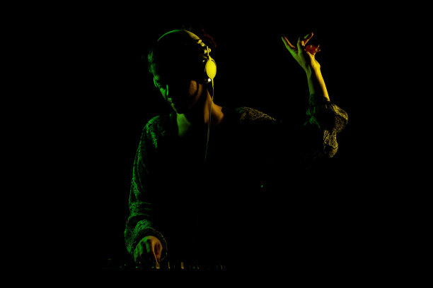 戴着耳机的女DJ。侧面点燃剪影的一个女孩玩电子音乐对黑色背景。图片下载