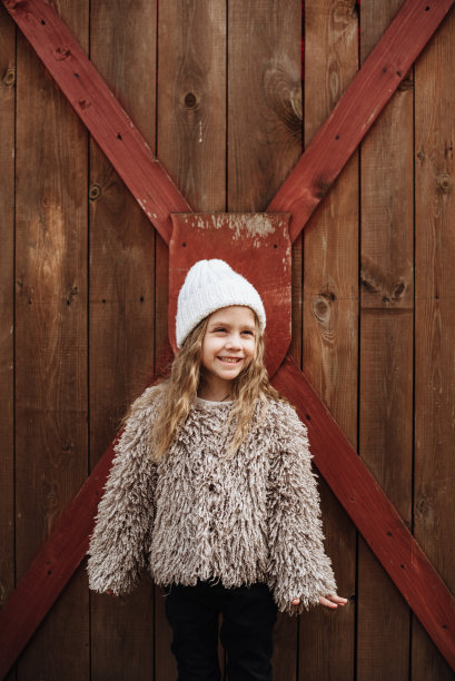 时髦的，四岁的长发女孩在木制背景上摆姿势。快乐宝宝的肖像。时尚照片。发短信的地方。图片下载