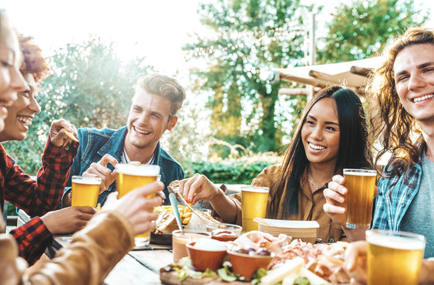 一群多民族的朋友一起在后院聚餐-千禧一代坐在酒吧的桌子上举杯在啤酒厂的花园-欢乐时光，午餐休息和青年的概念图片下载