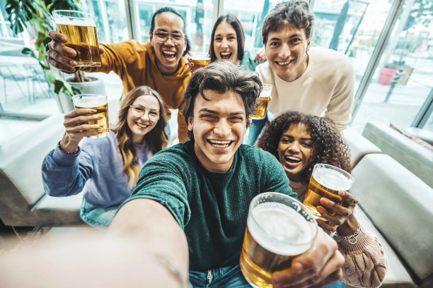 快乐的朋友在啤酒厂酒吧餐厅自拍照片-一群多种族的人享受欢乐时光喝啤酒坐在酒吧桌子-生活方式的概念与男孩和女孩出去图片下载