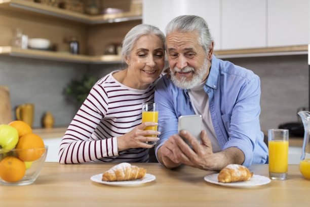 在厨房吃早餐时，快乐的老人夫妇使用智能手机的照片图片下载
