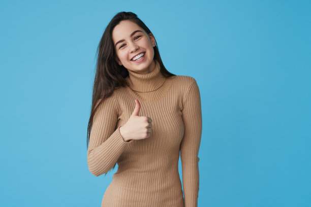 快乐的女士竖起大拇指，在蓝色的工作室微笑图片下载