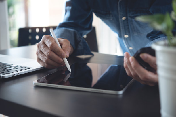 特写的休闲商务人士使用手写笔在数字平板电脑和笔记本电脑在办公桌上工作图片下载