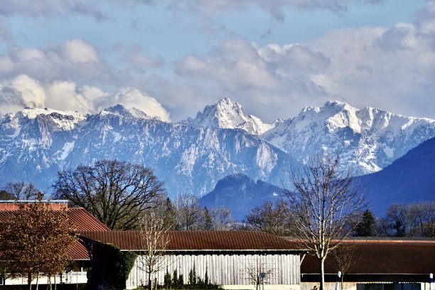 从巴伐利亚的一个小村庄的一侧看白雪皑皑的阿尔卑斯山。巴伐利亚北部的巴德艾布林镇。从村庄眺望白雪覆盖的阿尔卑斯山。白雪覆盖的阿尔卑斯山和脚下的绿草。图片下载