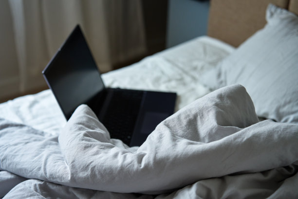 没有整理的床，枕头，皱皱的床单和打开的笔记本电脑图片下载