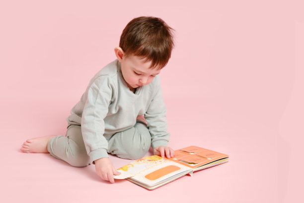 快乐的学步婴儿正在阅读一本书工作室粉红色的背景。小男孩在玩书。孩子一岁八个月，身高正常图片下载