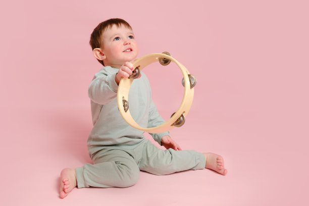 快乐的蹒跚学步的婴儿与乐器手鼓在工作室粉红色的背景。小男孩用打击乐器学习音乐。孩子一岁八个月，身高正常图片下载