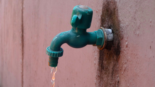 一个绿色的塑料水龙头连接在旧墙上。图片下载