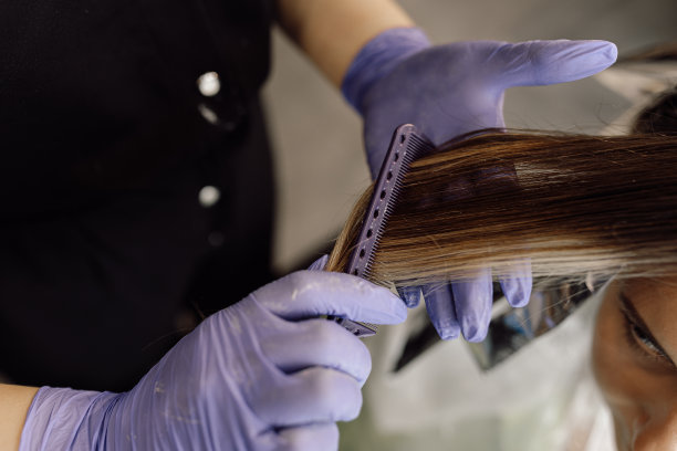 年轻女子坐在美容院的俯视图。面目全非的女子发型师染发梳染长发。图片下载