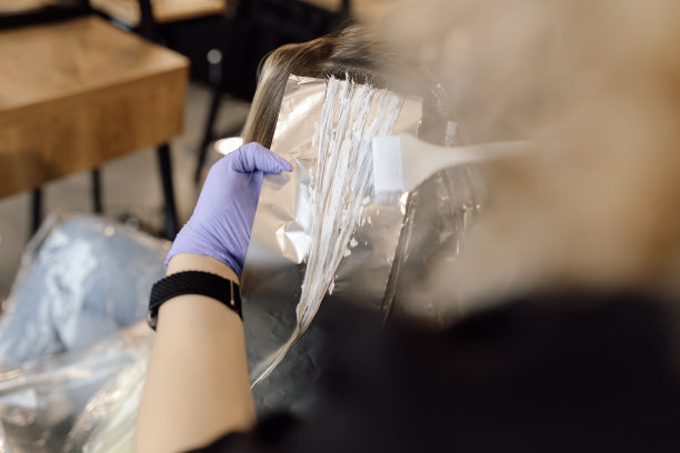 不认识的女人发型师染发师拿着一缕长头发在锡箔上，用刷子在手套上染发。图片下载