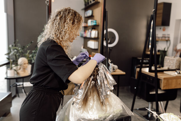 在美容院，戴着蓝色手套的发型师正在检查客户的头发颜色变化。发型。图片下载