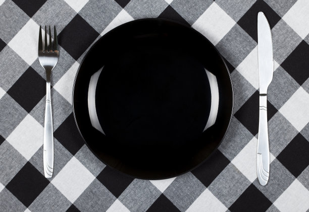 黑色的盘子，刀叉。盘子和餐具放在铺着格子布的桌子上图片下载