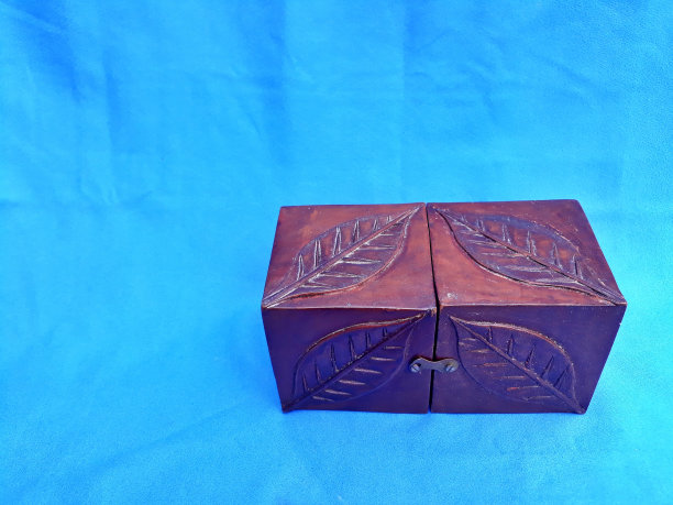 封闭的小木箱货架存储，如一个抽屉雕刻的树叶图案孤立在蓝色背景。静物装饰艺术图片下载
