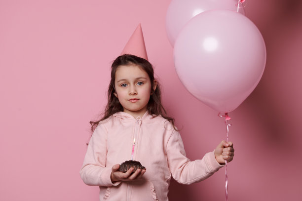 可爱的白人小孩女孩在粉红色的节日帽子，摆出生日纸杯蛋糕孤立的颜色背景图片下载